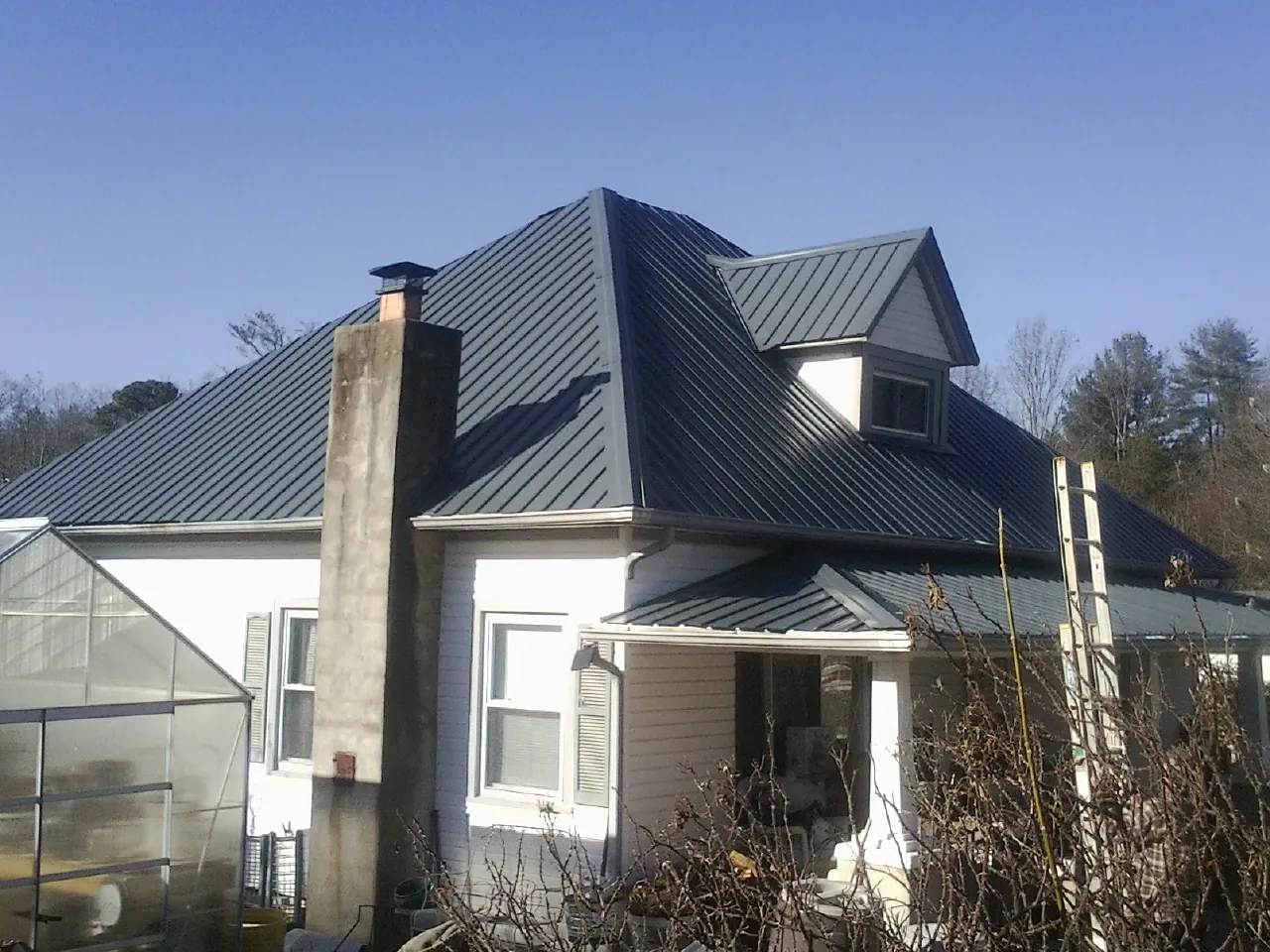Dark blue standing seam metal roof on a white farmhouse with dormer — Slate & Tile Roof Repair by Roofing Brothers in Lacombe