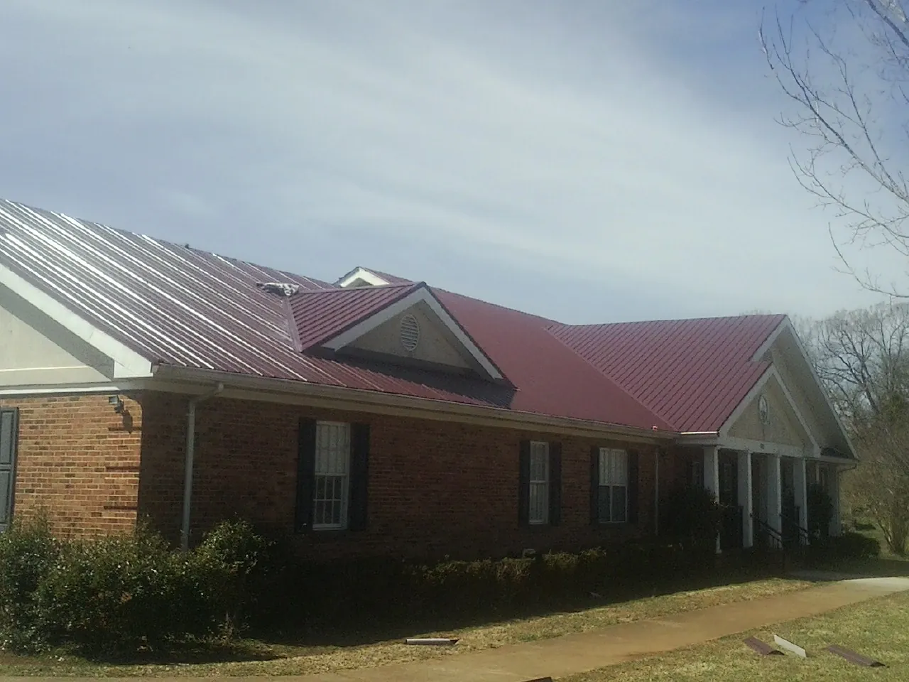 Red metal roof with gabled entries on a long brick building, from a Hail Damage Roof Repair job in Lacombe