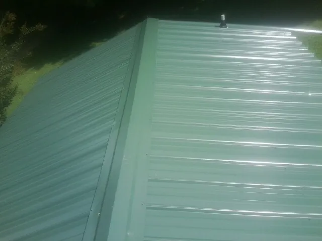 New green metal panels meeting at the ridge of a roof — Flat Roof Repair work by our crew in Lacombe