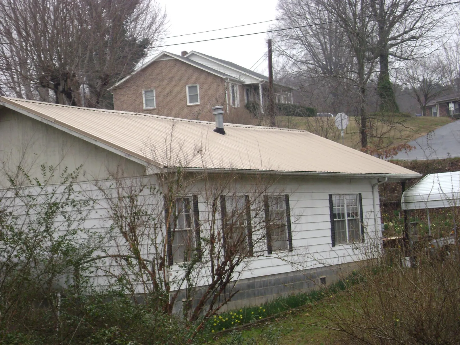 Tan metal roof on a white sided house set into a hillside — Commercial Roofing by Roofing Brothers in Lacombe