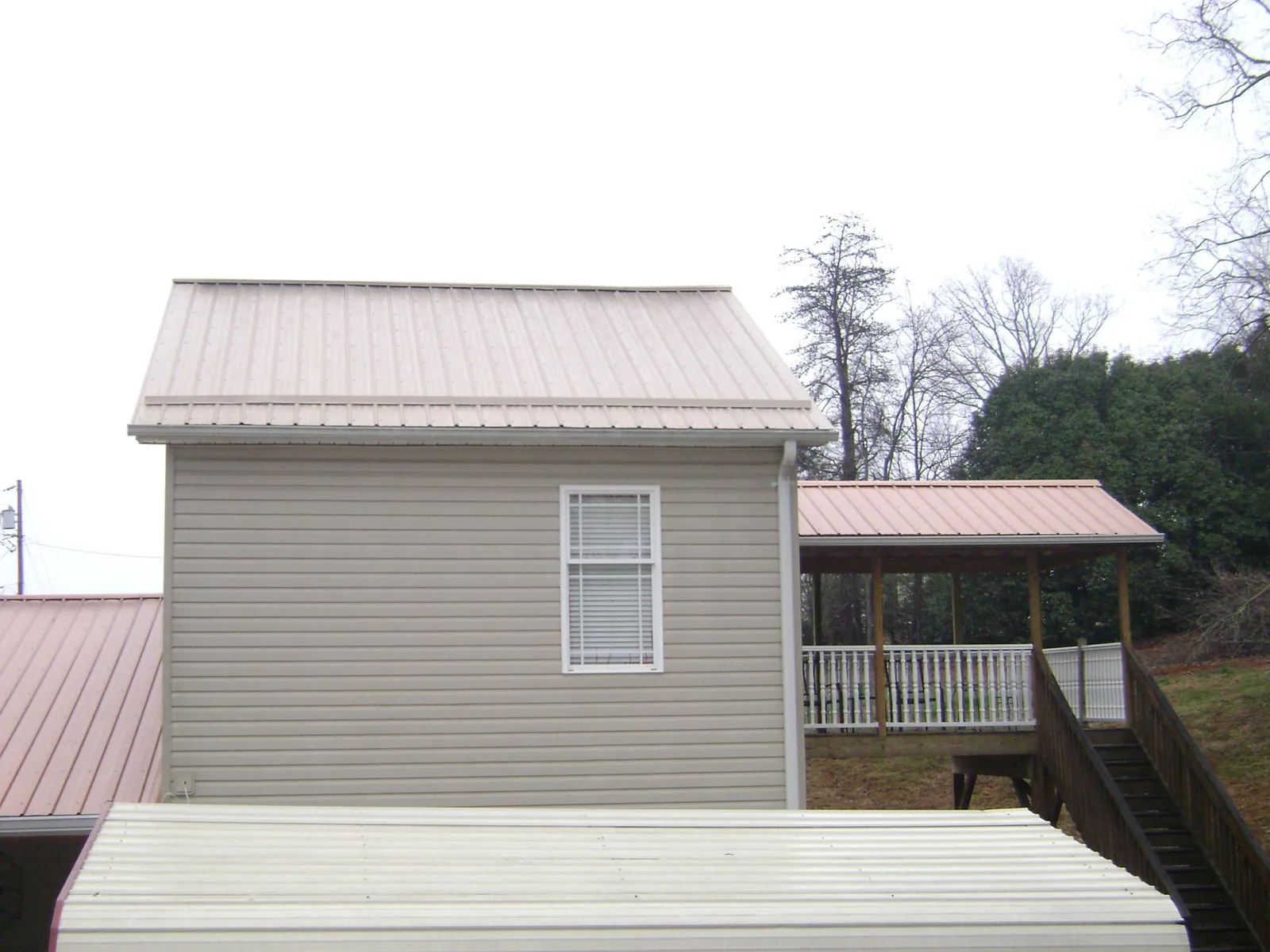 Tan metal roofs on a two story addition and attached porch, from a Roof Replacement job in Lacombe